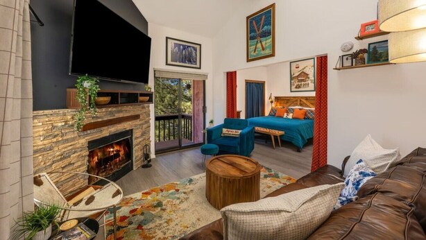 Una sala de estar con chimenea, televisor, sofá, un sillón azul y una cama con ropa de cama colorida.
