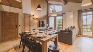 Uma sala de jantar com uma mesa de madeira, cadeiras e uma televisão fixada na parede.