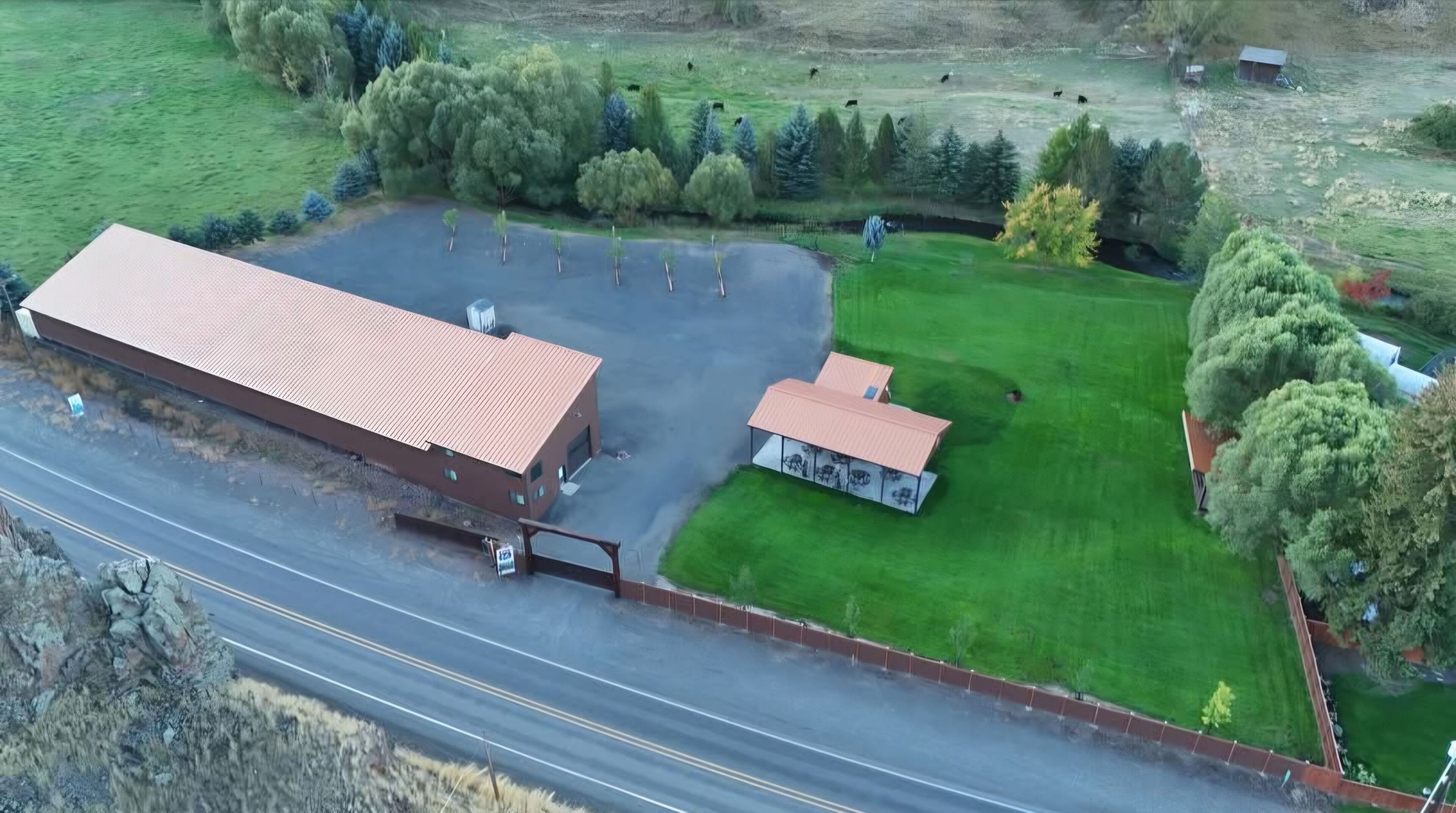 An aerial view of a building with a large parking lot, a smaller structure, and a well-maintained lawn.