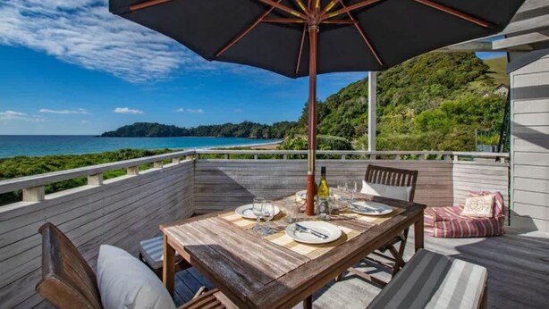 Un pontile in legno con un tavolo apparecchiato per mangiare, un ombrellone grande e vista sull'oceano.