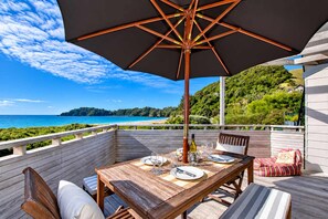 Eine Holzterrasse mit Esstisch, mit Blick auf Strand und Meer.
