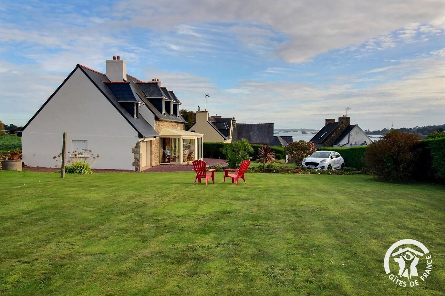 Une maison avec une grande pelouse, un patio couvert et une vue sur la mer.
