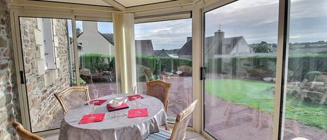 Ein Wintergarten mit Esstisch, Korbstühlen und Blick auf Garten und Gebäude.
