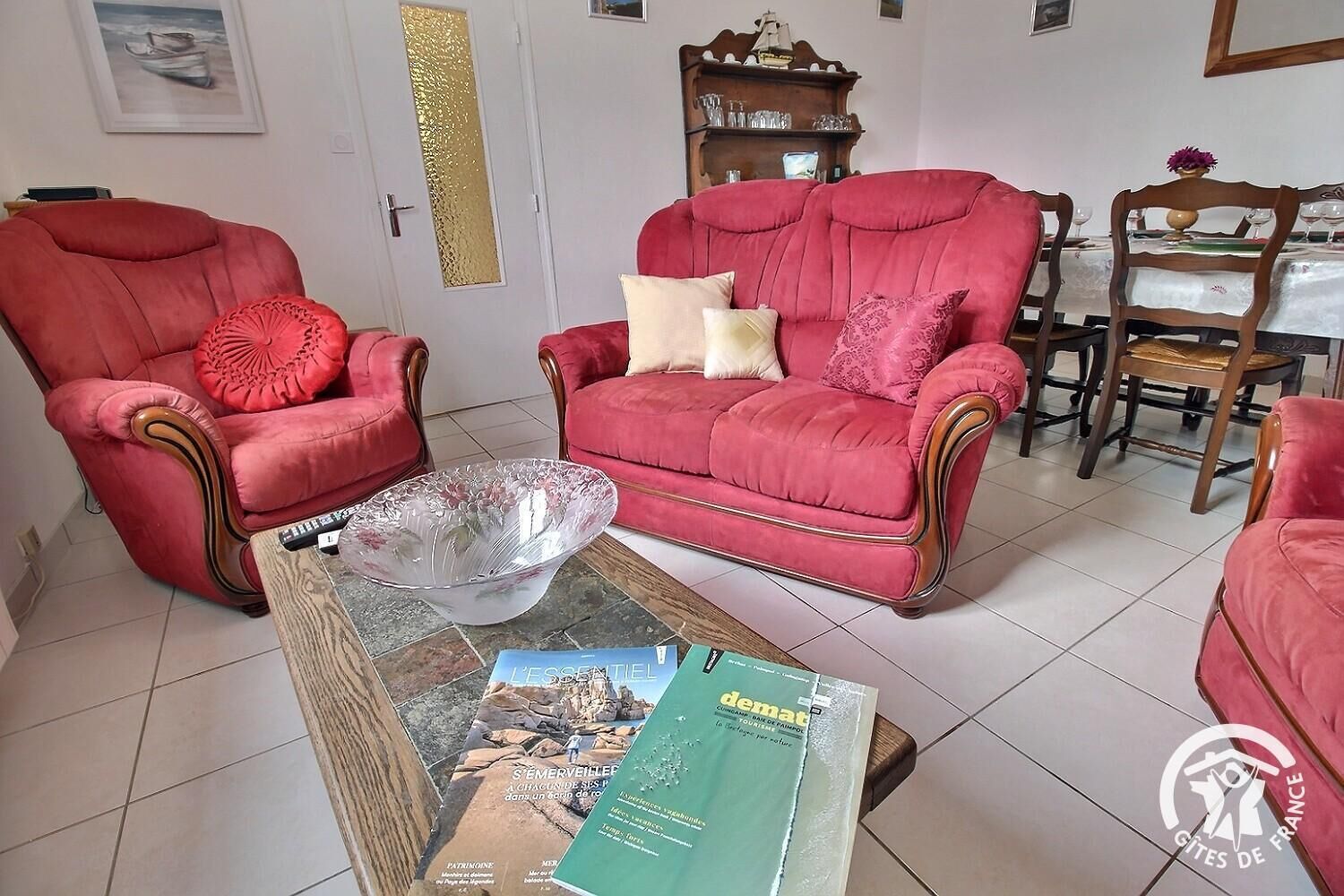 A living room with a red sofa, a glass coffee table, and a dining area with a table set for two.