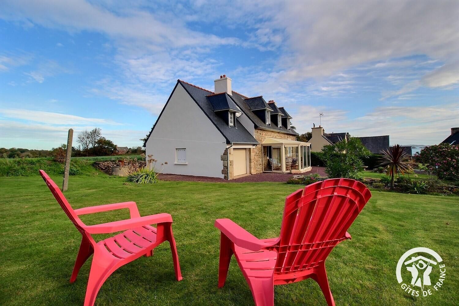 A house with a large lawn, two red chairs, and a glass door leading to a covered porch.