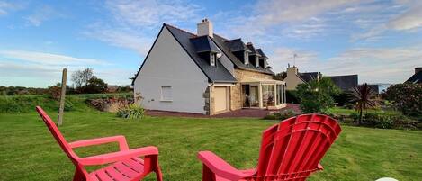 A house with a large lawn, two red chairs, and a glass door leading to a covered porch.