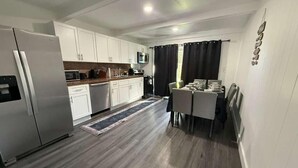 A modern kitchen with white cabinets, a stainless steel refrigerator, a microwave, and a dining area with a table and chairs.