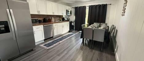 Una cocina moderna con armarios blancos, un refrigerador de acero inoxidable, un microondas y un comedor con mesa y sillas.