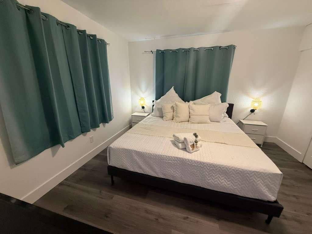 Una cama bien tendida con ropa blanca, dos lámparas de noche y cortinas color turquesa.