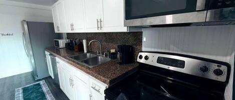 A modern kitchen with white cabinets, a stainless steel microwave, a black oven, and a granite countertop.