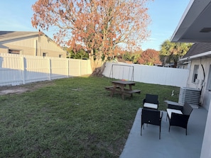 Un jardin avec une table de pique-nique et des chaises, une balançoire et une clÎture blanche.