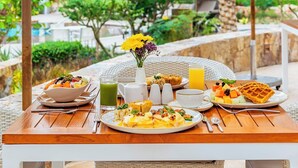 A dining table set with breakfast items, including waffles, fruit, and a green drink, under a canopy with a view of a building and greenery. - 2-bedroom Beach Resort Villa La Valencia in the heart of Los Cabos with gym (San José del Cabo)