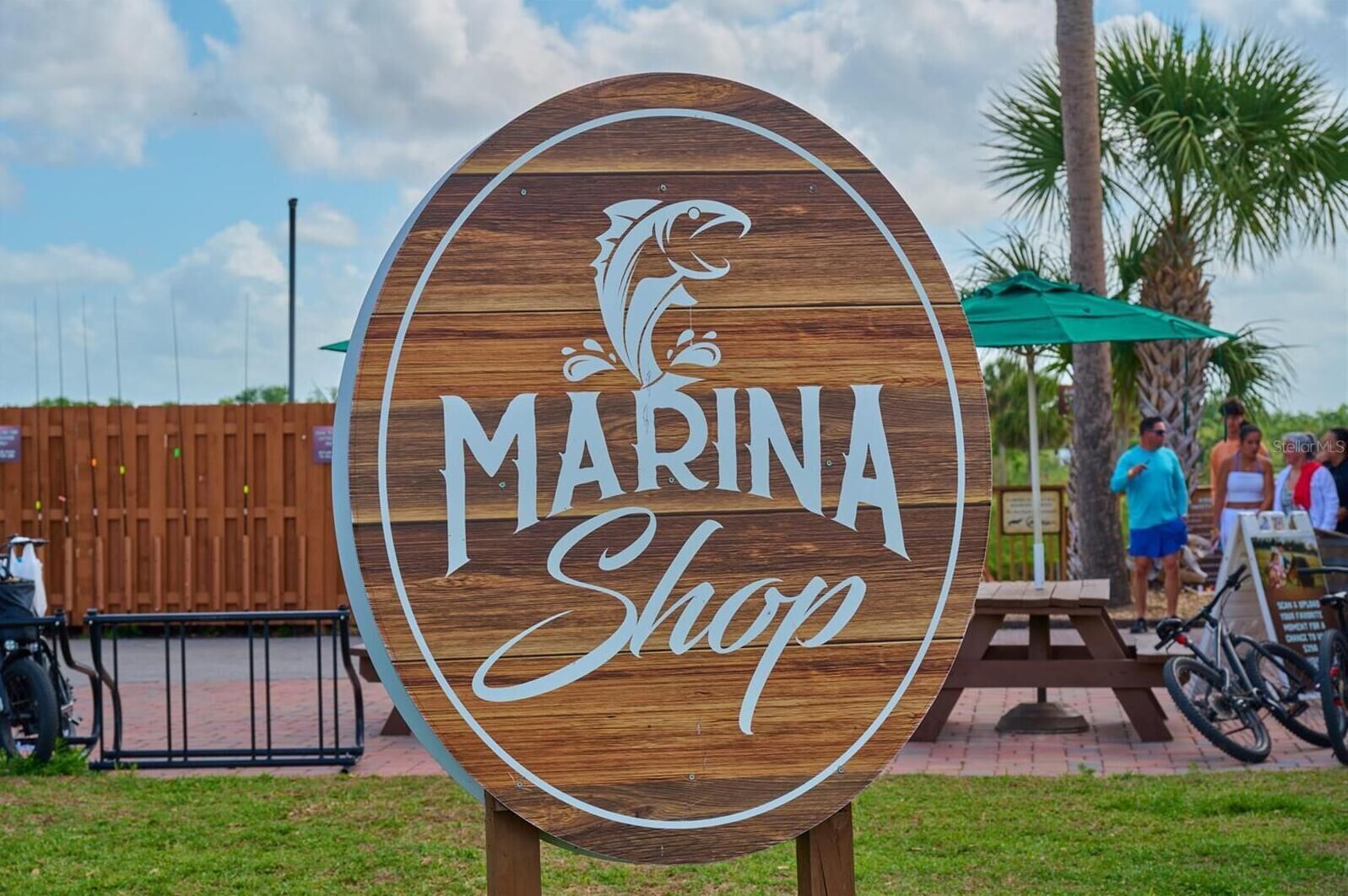 Une enseigne en bois portant l’inscription « MARINA Shop » et un logo représentant un poisson stylisé.