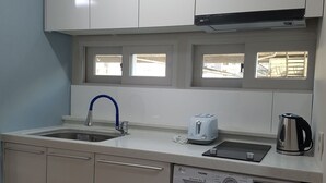 Una cocina compacta con armarios blancos, lavavajillas integrado, lavadora, tostadora y hervidor.