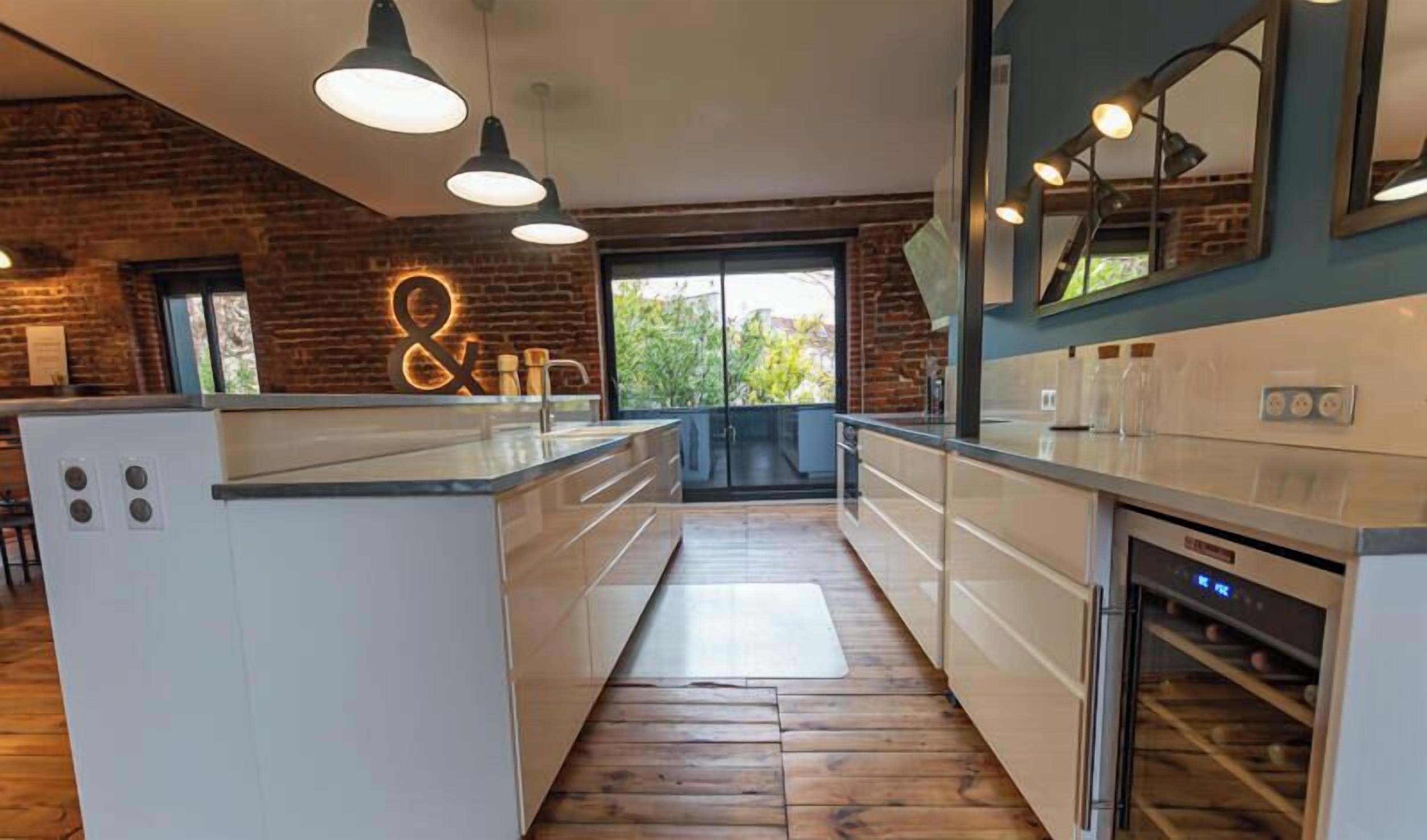 Une cuisine moderne avec un îlot central, des luminaires suspendus et un mur en briques.