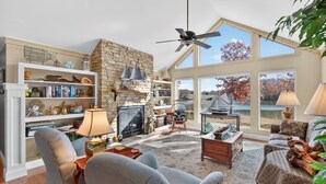 A spacious living room with a fireplace, bookshelves, and a large window with a view of a lake. - Waterfront Lake Anna Private Side Retreat + Boathouse Oasis (Mineral)
