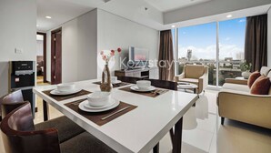Una sala de estar moderna con comedor, ventanas amplias que ofrecen vistas a la ciudad, televisor de pantalla plana y dispensador de agua.