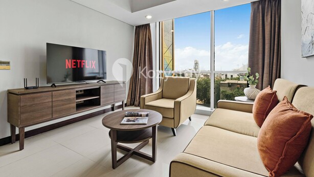 Una sala de estar moderna con una televisión de pantalla plana, un sofá, una mesa de centro y vistas de la ciudad a través de amplias ventanas.