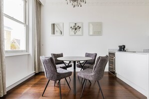 Cozinha moderna com mesa redonda e quatro cadeiras cinzas estofadas, armários brancos e um candelabro.