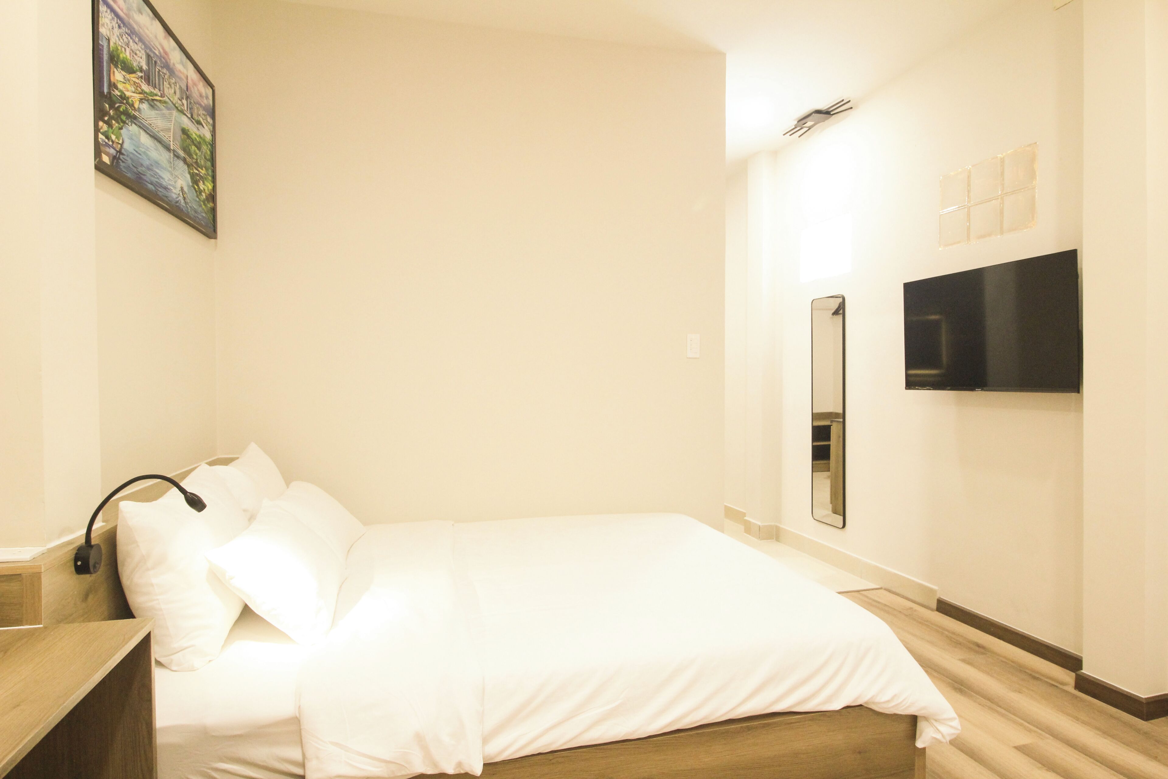 Une chambre d’hôtel avec un lit, une table de chevet, un téléviseur fixé au mur et un tableau.