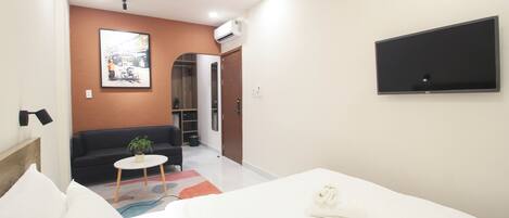 Una habitación de hotel moderna con una cama, un sofá, una mesita con una planta y un televisor en la pared.