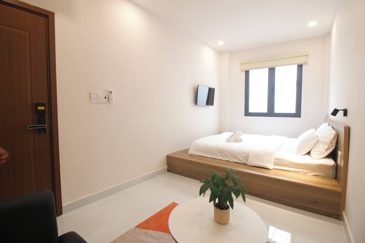 A modern bedroom with a bed, a bedside table with a plant, a window, and a door.