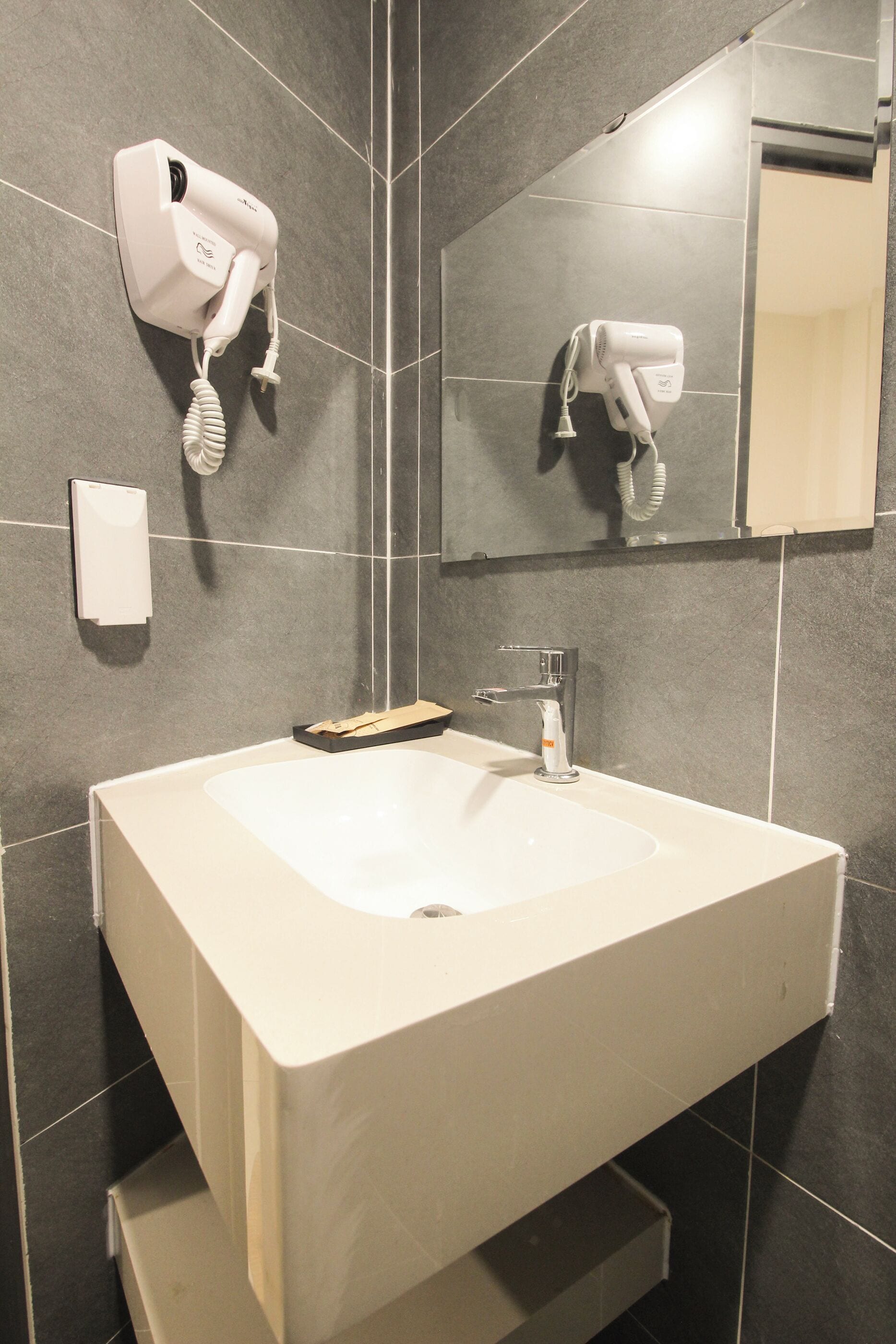 A bathroom with a white sink, a mirror, and a hairdryer mounted on the wall.