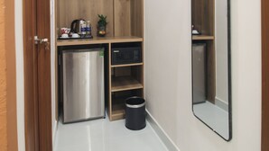 A narrow hallway with a built-in closet, a small refrigerator, and a trash bin. - De Lustora Hotel & Apartment - District 1, HCM. (Ho Chi Minh City)