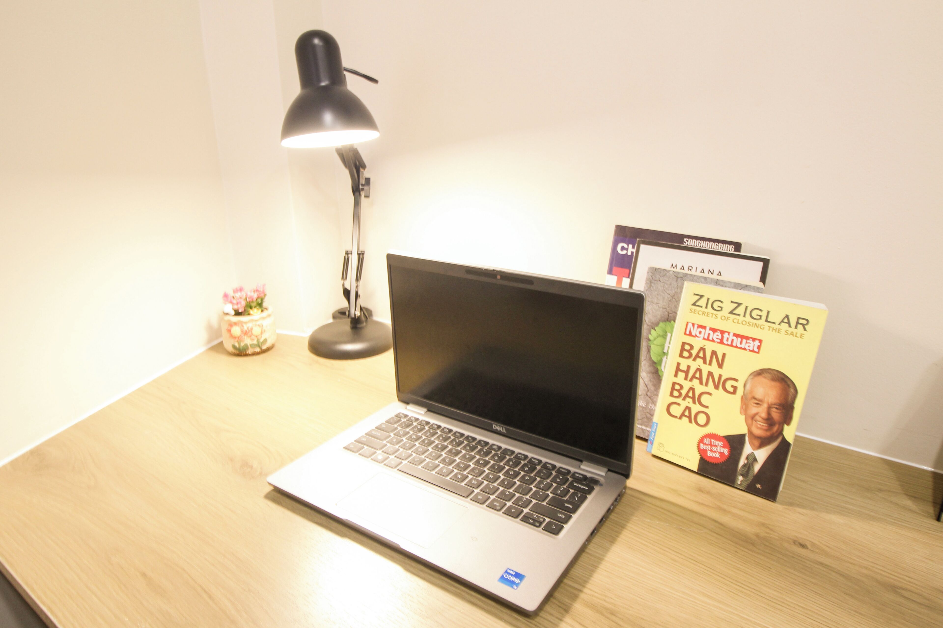 Ein Laptop auf einem Holztisch mit Lampe und Büchern.