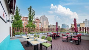 An outdoor patio with tables and chairs, a wooden deck, and a view of buildings in the background. - The Garden F (Shanghai)