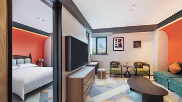 A modern hotel room with a bed, a TV, a sofa, and a coffee table.