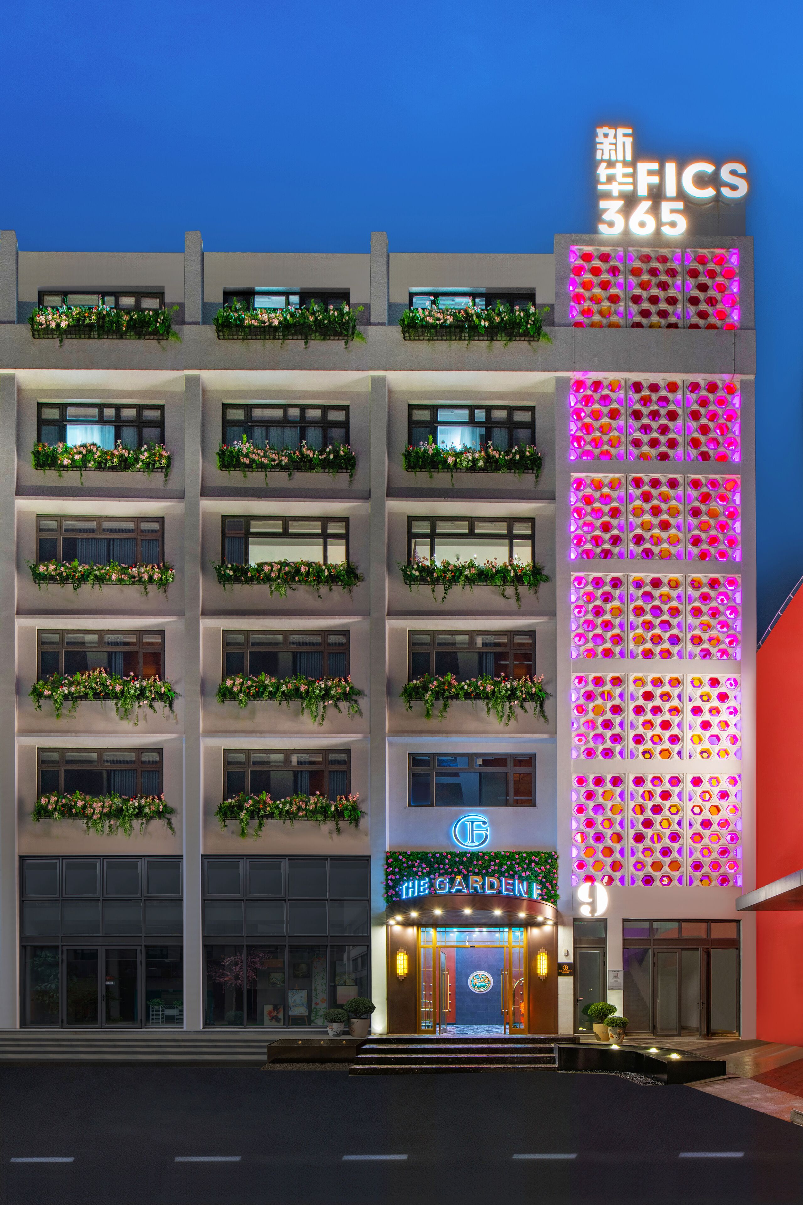 A hotel with multiple floors, balconies with greenery, a brightly lit entrance, and a neon sign.
