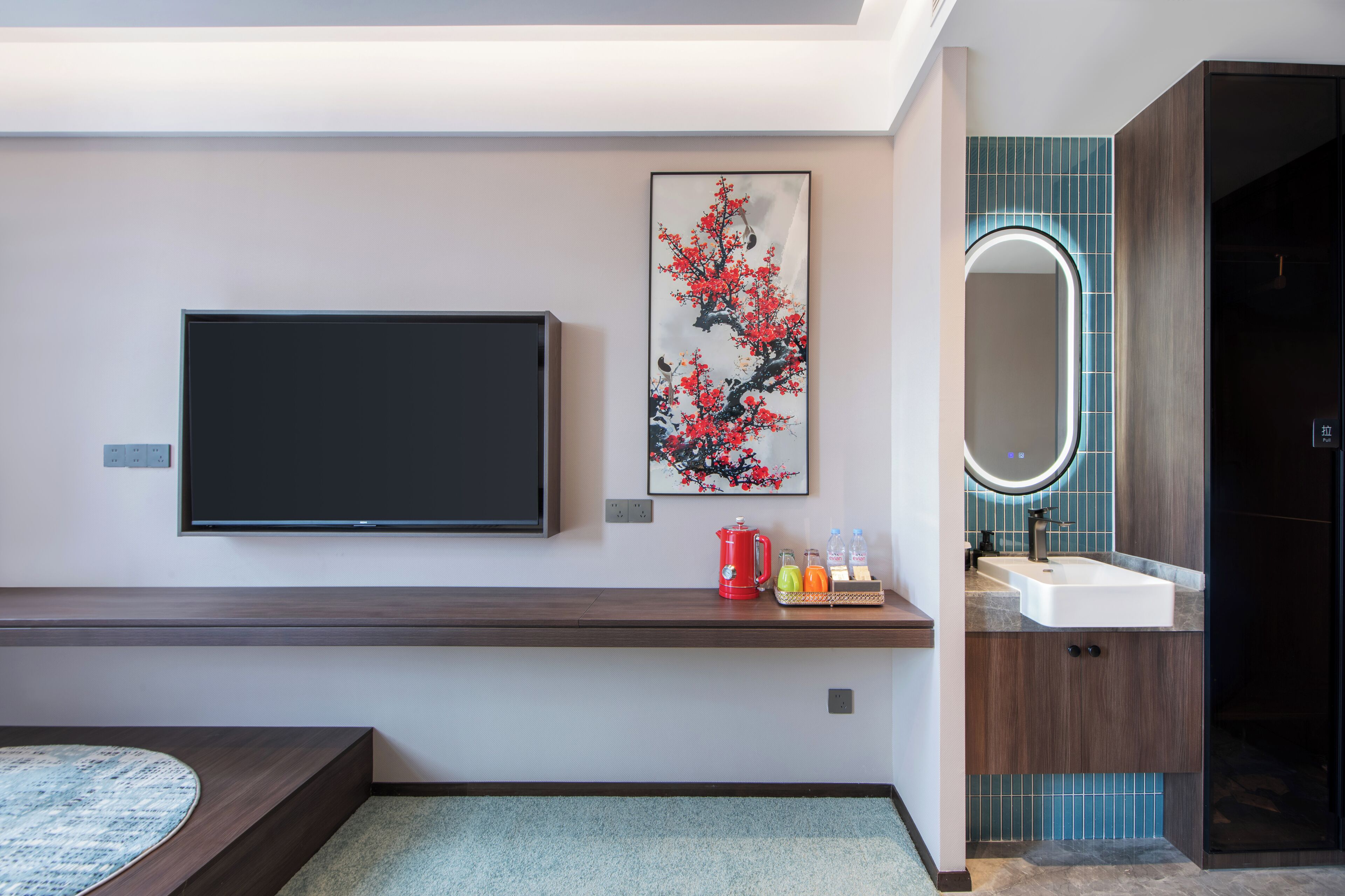 A modern bathroom with a mounted TV, a decorative painting, a coffee maker, and a sink with a mirror.