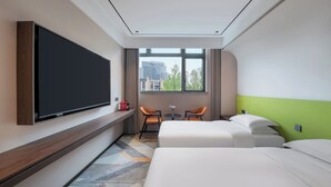 A hotel room with a large flat-screen TV mounted on the wall, two single beds, a small table with two chairs, and a window with a view of buildings and trees. - The Garden F (Shanghai)