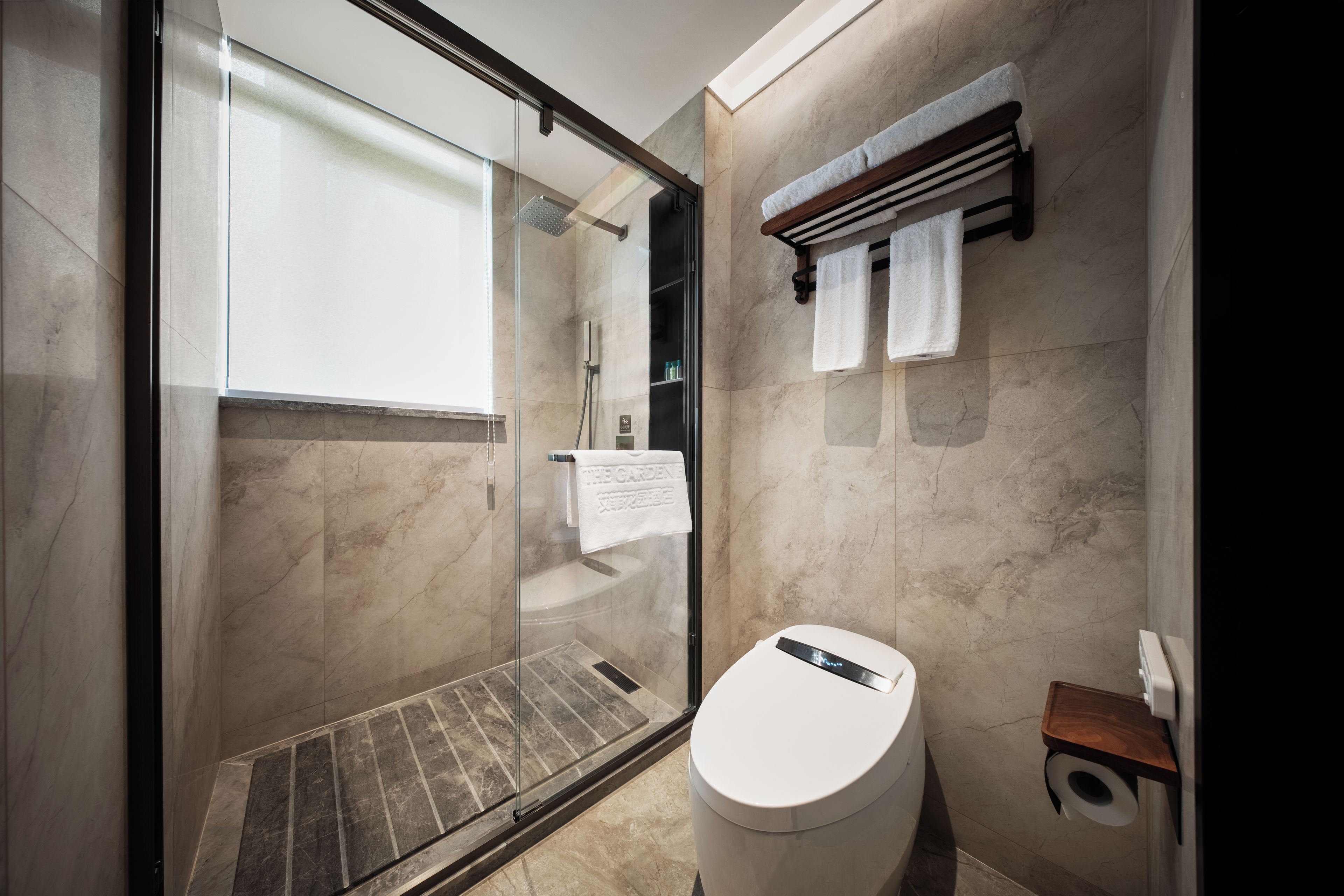 A modern bathroom with a glass-enclosed shower, a toilet, and a towel rack.