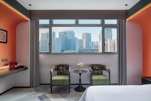 A hotel room with a large window, two upholstered chairs, a small round table, and a bed.