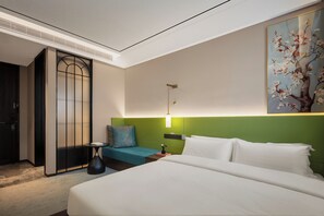 A hotel room with a bed, a nightstand, a lamp, a painting, and a door with a frosted glass panel. - The Garden F (Shanghai)