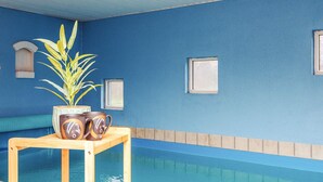Zona de piscina con una mesa de madera que sostiene una planta en maceta y dos tazas decorativas.