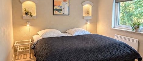 A bedroom with a bed, two wall-mounted lights, a window, and a framed picture on the wall.