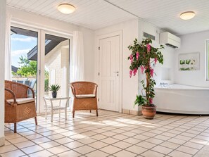 A room with a tiled floor, two wicker chairs, a potted plant, a white door, and an air conditioning unit. - 12 Person Holiday Home in Oksbol (Oksbol)