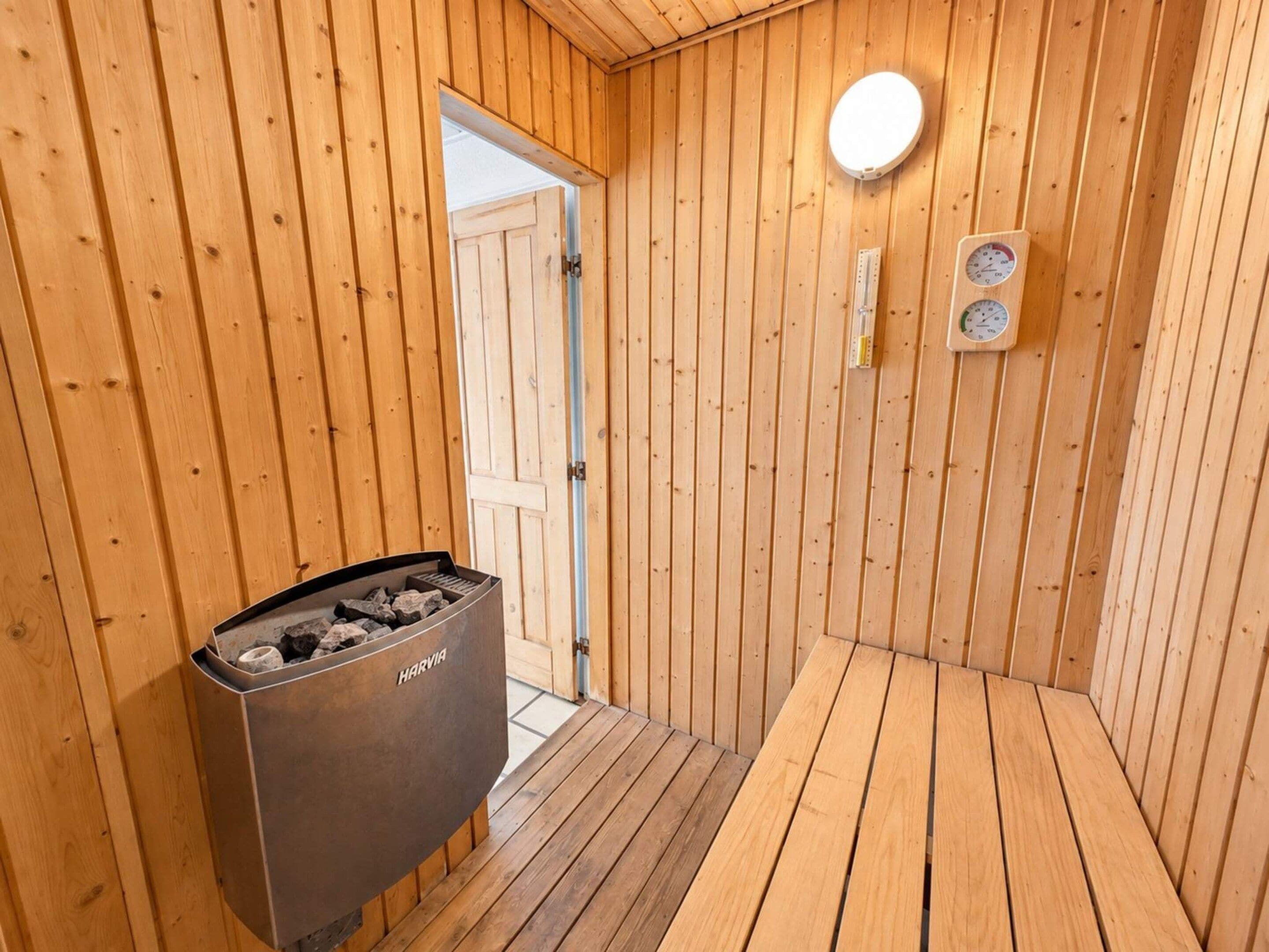 Uma sala de sauna de madeira com porta, termômetro fixado na parede e lixeira com a etiqueta 'HARVIA'.