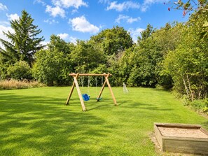 A wooden swing set in a grassy yard with a hedge and trees in the background. - 12 Person Holiday Home in Oksbol (Oksbol)