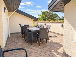 Een terras buiten met een tafel en stoelen, een metselstenen vloer en een muur met een raam.