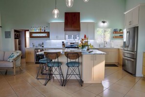 Una cocina moderna con una isla central, taburetes de bar, un refrigerador y un área de comedor con un sofá.