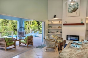 A spacious living area with a pool, outdoor seating, a fireplace, and a large window overlooking greenery. - Ocean View Retreat- Mountain Top, Heated Pool, Generator (St Thomas)