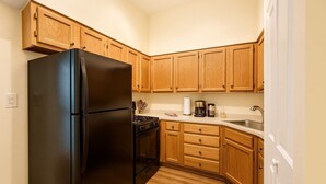 Una cocina compacta con armarios de madera, un refrigerador negro, una estufa y un lavamanos.
