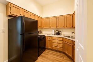 Una cocina compacta con armarios de madera, un refrigerador negro, una estufa y un lavamanos.