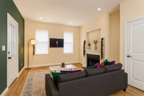 Ein Wohnzimmer mit Sofa, Couchtisch, Stehlampe, Kamin und einem an der Wand befestigten Fernseher.
