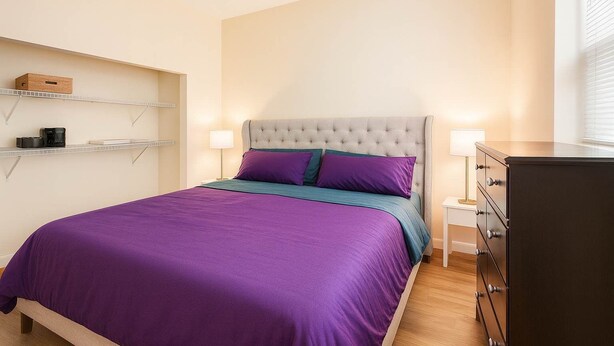 Un dormitorio ordenado con cama, mesitas de noche, cómoda y estanterías con objetos.
