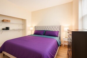 Ein ordentlich eingerichtetes Schlafzimmer mit Bett, Nachttischen, einer Kommode und Regalen mit Gegenständen.